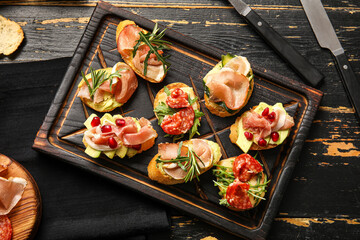 Board of tasty bruschettas with ham on dark wooden background