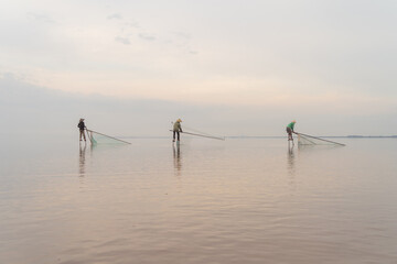 Silhouette of Vietnamese fisherman holding a net for catching freshwater fish in nature lake or river with reflection in morning time in Asia in Vietnam. People.