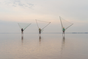 Silhouette of Vietnamese fisherman holding a net for catching freshwater fish in nature lake or...