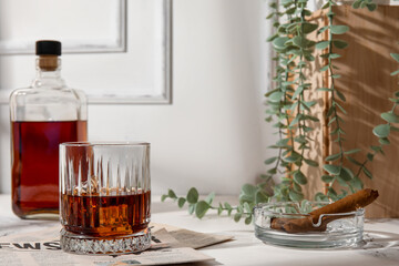 Glass of cold rum, newspaper and ash tray with cigar on table