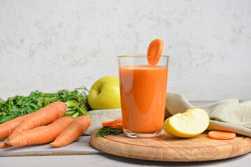 Board with glass of tasty carrot juice on wooden table