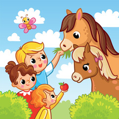 Cute children feed grass and apples to horses and foals.