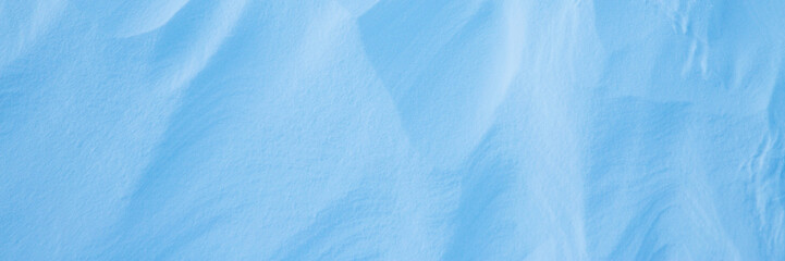Beautiful winter background with snowy ground. Natural snow texture. Wind sculpted patterns on snow surface. Wide panoramic texture for background and design.