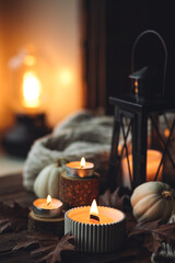 Cozy autumn composition with aromatic candle, pumpkins, wool sweater, leaves, cinnamon. Aromatherapy on a grey fall morning, home atmosphere of cosiness and relax. Wooden background close up.