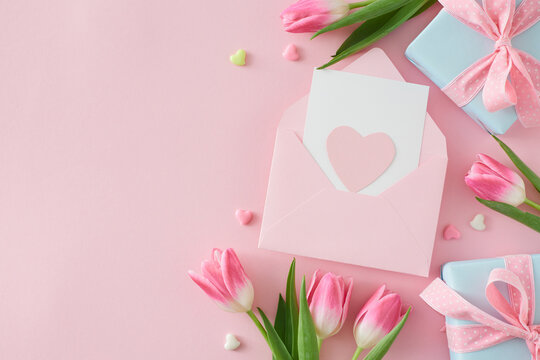 Flat lay photo of postcard with heart gift boxes pink tulips flowers and colorful hearts on isolated pastel pink background with copyspace. Happy Mother Day concept.