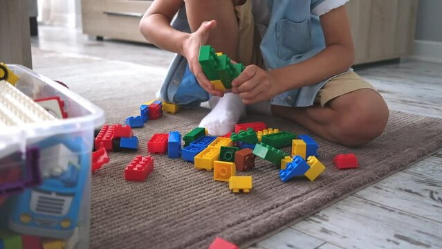 Little toddler boy playing with colorful plastic blocks at home living room on carpet building creative game, imagination