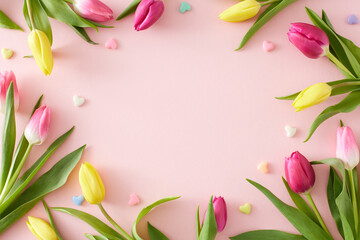 Top view composition of yellow pink tulips flowers and colorful hearts baubles on isolated pastel pink background with blank space in the middle. Happy Mother's Day idea