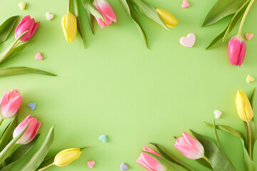 Fototapeta na wymiar Top view composition of colorful tulips flowers and hearts baubles on isolated light green background with empty space in the middle. Happy Mother's Day concept