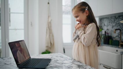 Lovely child waving laptop at kitchen close up. Happy daughter speaking remotely