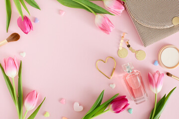 Obraz na płótnie Canvas Flat lay composition of perfume bottle handbag bijouterie earrings cosmetic powder and brushes and tulips flowers on pastel pink background with blank space. Mother Day mood concept