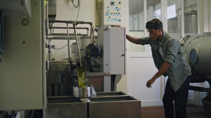 Serious man turning press machine at fabric closeup. Worker producing olive oil