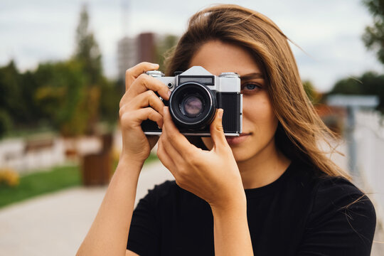 Close up shot of a beautiful young woman taking a photo with a vintage camera outdoors.