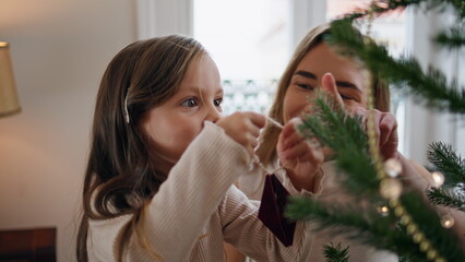 Cute child decorating Xmas tree with mom home closeup. Mother embracing daughter