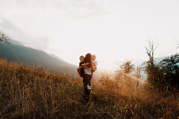 mother with children walk across a field among the mountains in the beautiful sunset light on a...