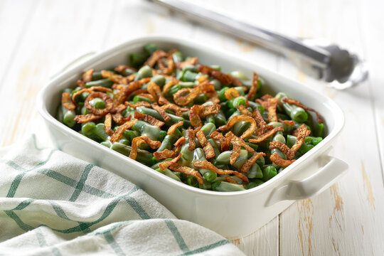 green bean casserole with crispy fried shallots onions on a white wooden table.