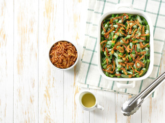 green bean casserole with crispy fried shallots and cream sauce on a white wooden table top view with copy space for text.