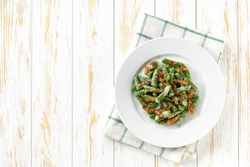 Oven baked green bean casserole sprinkled with crispy fried onions , in white plate on a light wooden table, copy space for text.