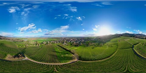 360 panorama aerial drone view above the Uffholtz and Wattwiller villages green vineyard hills in a Alsatian valley by sunny day with blue sky, dark stormy clouds in the distance, with paths