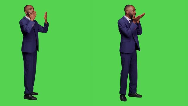 Optimistic startup manager sending air kisses in studio, standing over full body greenscreen, doing romantic gesture. Male employee in office suit with kissy face being positive and cheerful.