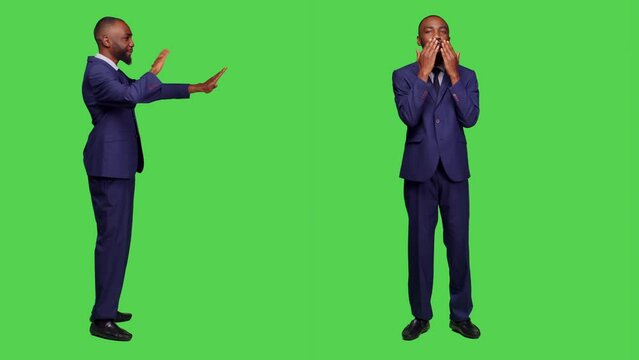 Cheerful romantic office worker sending air kisses posing over full body green screen backdrop, doing optimistic gesture. Young man in formal suit with kissy face being positive and confident.