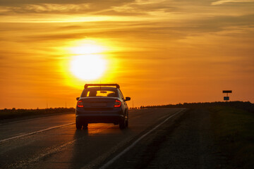 Fototapeta na wymiar The silhouette of a car on the road against the background of the sun. The car is driving on the highway during sunset. The concept of travel and freedom.
