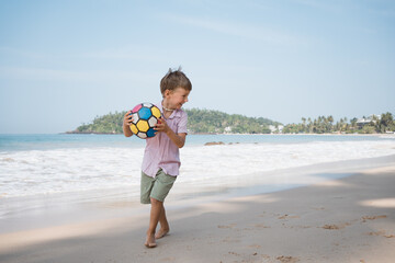 Little blond boy playing ball at the beach of sea cost at summer day