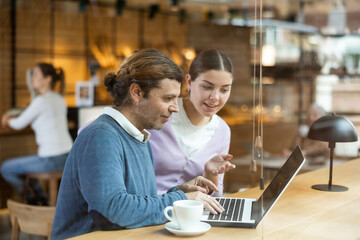 Confident male and female cafe customer enjoying coffee while working on laptop