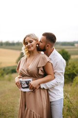 Pregnant woman with husband holding ultrasound baby image. Close-up photo of ultrasound image on the background of a pregnant belly in the hands of mother and father. The concept of pregnancy.