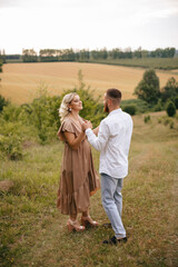 A man is holding hands his pregnant wife in a field at sunset.