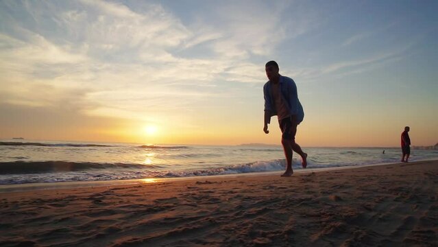 A male athlete is making back flip and lands on feet on the sandy tropical beach at sunset, slow motion