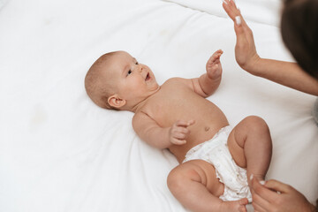 Newborn baby giving high-five to mom on a white blanket. 