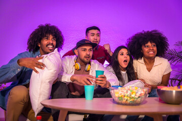 Adult party. Young people sitting on the sofa watching a football game with popcorn. Excitement for soccer, purple led, nervous in the last minutes for the game