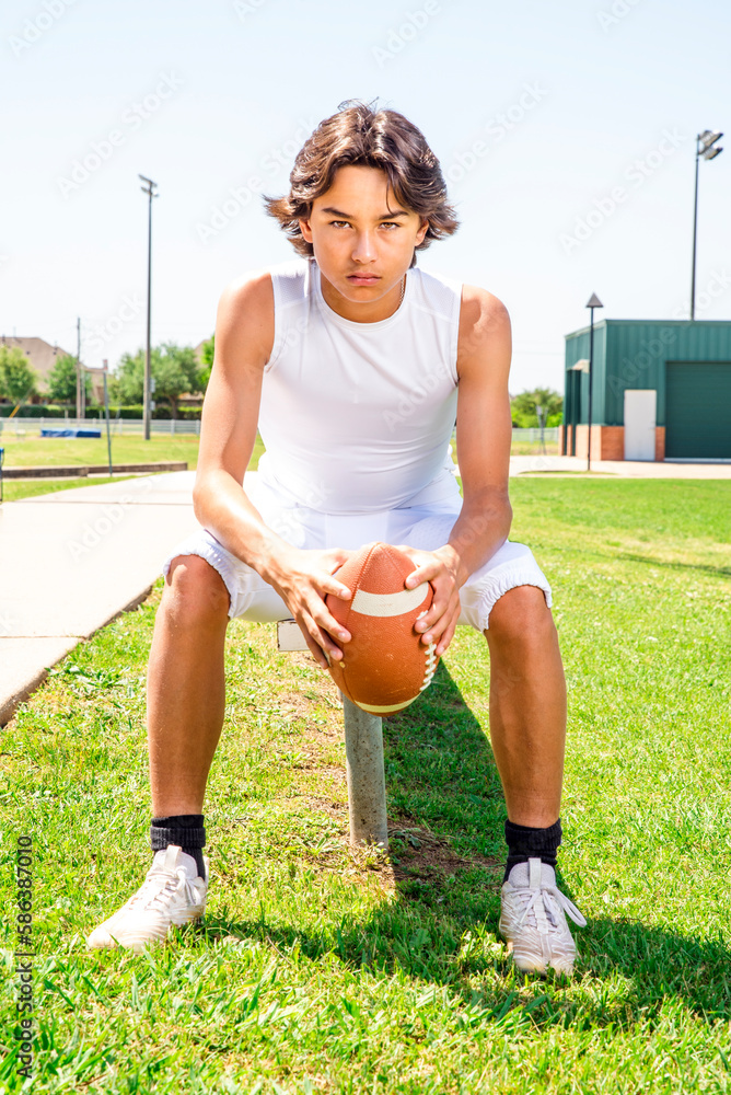 Wall mural Young teenage football player in uniform sitting on bench sunny outside