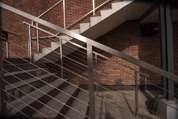 Dizajnerskie schodki z poręczami z profilów ze stali nierdzewnej i stalowych linek . Ściana z czerwonej cegły klinkierowej .