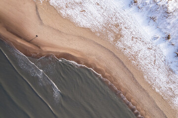 Man walking Winter in cold Baltic sea snowy beach in Gdansk. Aerial view of snow covered beach and...