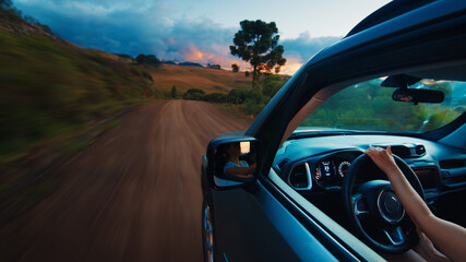 Woman steers the car on a rural road at vivid sunset. Solo female traveler drives the car on an...