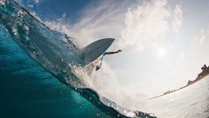 Pro surfer rides the wave. Young man surfs the ocean wave in the Maldives and aggressively turns on the lip. Splitted above and underwater view - 586389680
