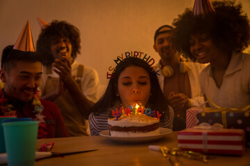 Multi-ethnic group of friends at a birthday party on the sofa at home with a cake and gifts,...