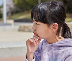 Fototapeta na wymiar 春の公園でベンチに座って思考している小学生の女の子の姿