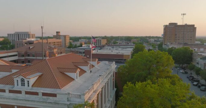 Aerial Panning Shot Of National Flags Waving On Roofed Structure In City During Sunset - Tuscaloosa, Alabama