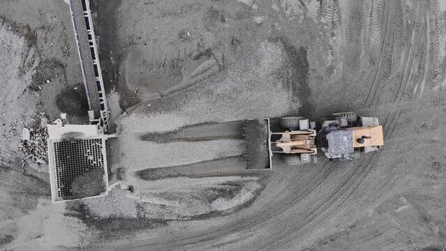 Backhoe pours gravel into sorter of rock crusher system at extraction quarry upper view. Natural deposits processing in pit
