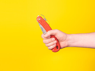 A hand holds a folded pruning saw. No face, yellow background, copy space.
