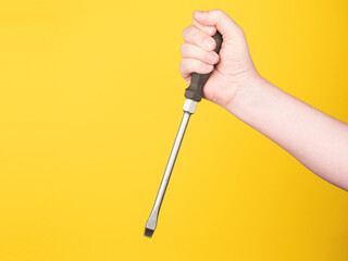 A male hand is holding a very large screwdriver. Yellow background, no face. Concept. 
