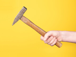 A hand is holding a hammer against a yellow background. No face, copy space, concept.
