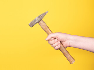 A hand is holding a hammer against a yellow background. No face, copy space, concept.
