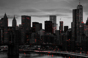 Red lights shining in black and white night time cityscape with the Brooklyn Bridge and buildings of Manhattan in New York City