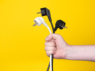 A male hand holds three electric plugs. No face, yellow background, copy space.
