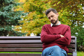 Tired man sleeping on bench in beautiful green park. Space for text