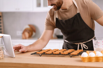 Man with freshly baked cookies watching online cooking course via tablet in kitchen, closeup