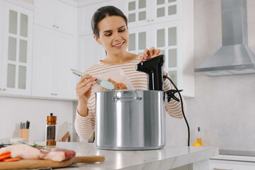 Woman putting vacuum packed meat into pot and using thermal immersion circulator. Sous vide cooking